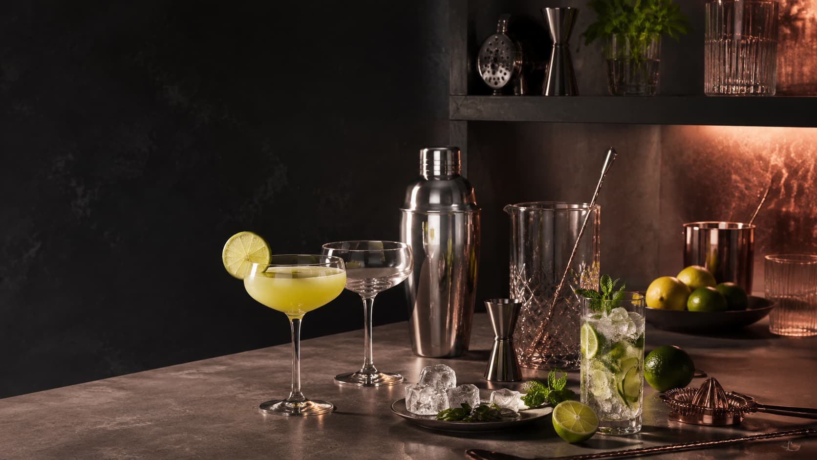 Polished home bar tools, glassware and citrus arranged on a moody residential bar